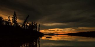 a solo person paddles while canoe tripping through the dusk light