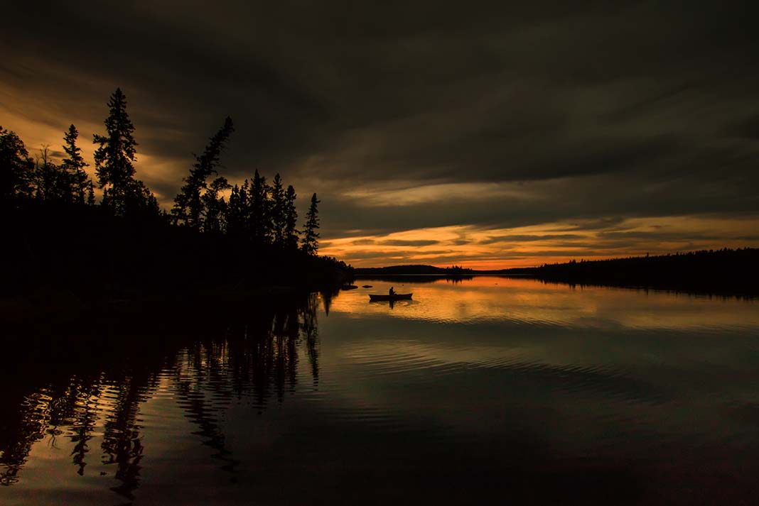 a solo person paddles while canoe tripping through the dusk light