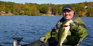 man holds up bass caught from a kayak after organizing his tackle boxes