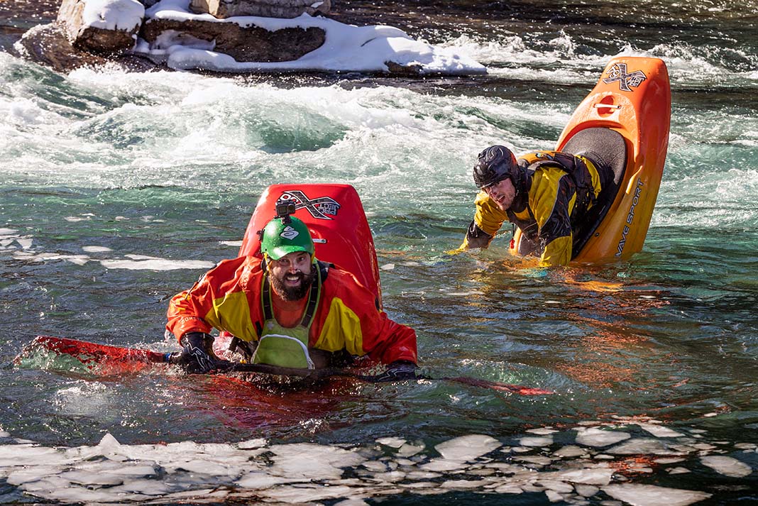 two male whitewater kayakers demonstrate the kayak bow stall in an icy river