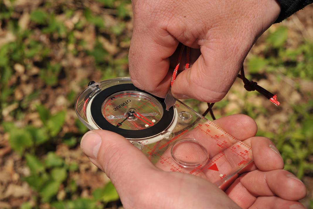 Hands using a key to set declination on the back of a compass.