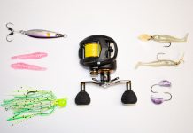 A selection of saltwater fishing lures and a reel laid out on a white background