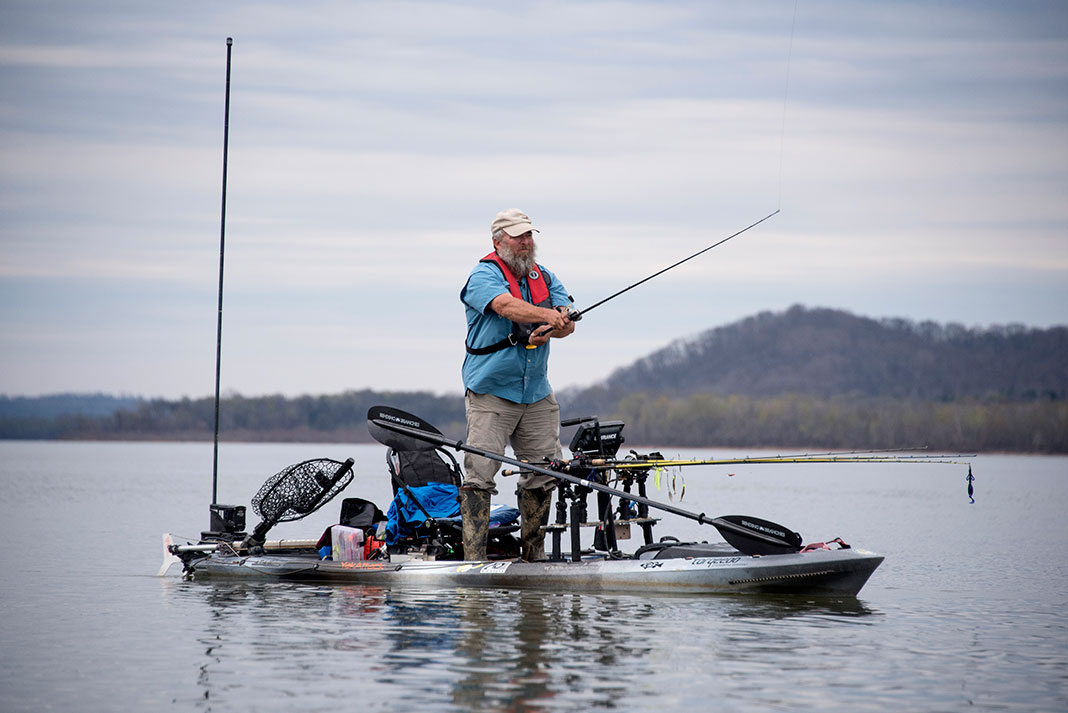 man casts from a Wilderness Systems ATAK 140 fishing kayak