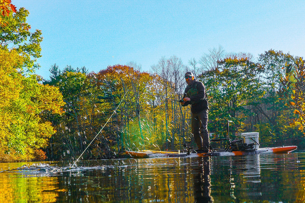 angler stands up and fishes for bass from a kayak in the fall season