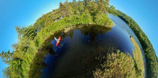 fisheye photo of an angler standing up and fishing from a kayak surrounded by trees