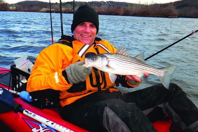Eric Harrison holds a striped bass in his kayak. | Photo: Pat Gallagher