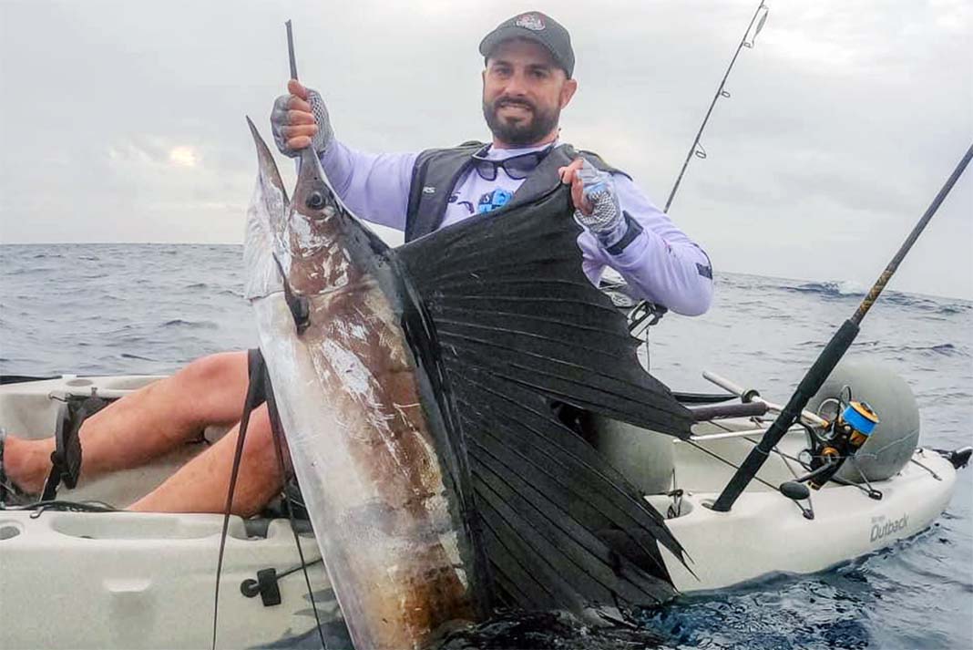man poses with sailfish after it spears his kayak