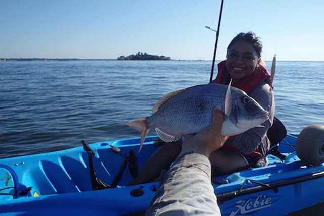 woman poses for photo with a fish she caught by kayak
