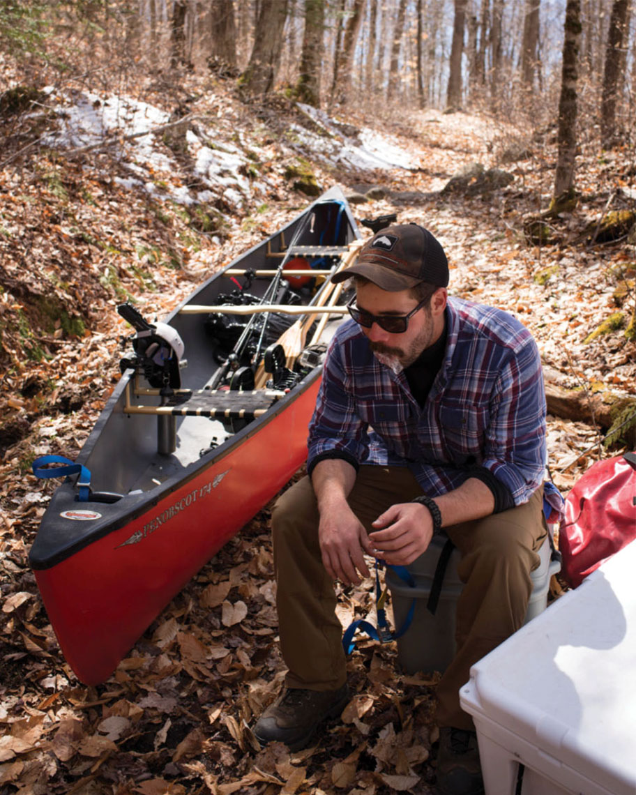 man rests in the Adirondacks forest after portaging a canoe
