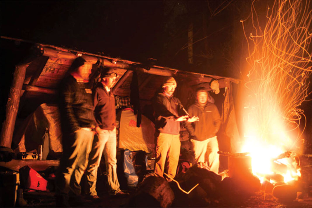 a group of men stand before a large fire warming their hands