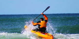 man launches a paddle kayak through surf