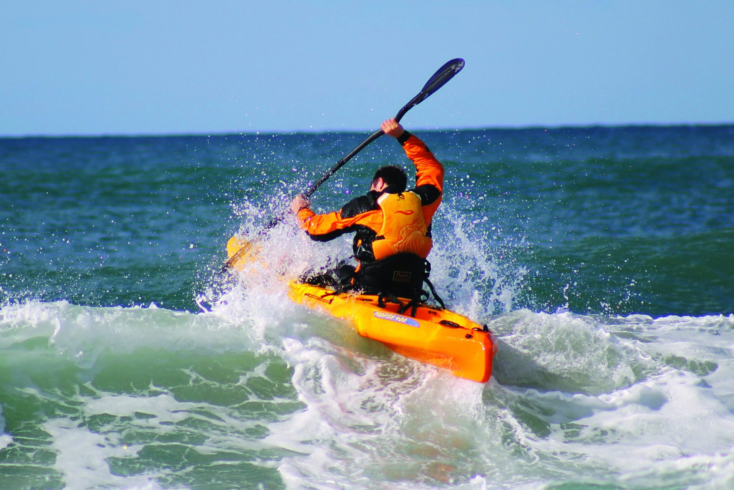 man launches a paddle kayak through surf