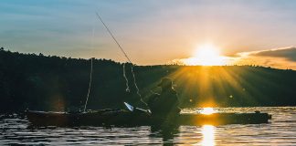 kayak angler casts while silhouetted in dawn light