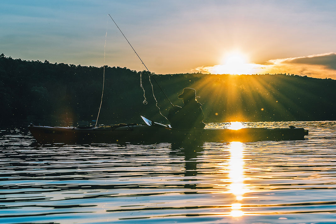 kayak angler casts while silhouetted in dawn light