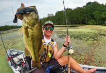 man holds up a largemouth bass caught from a kayak with a swimbait lure