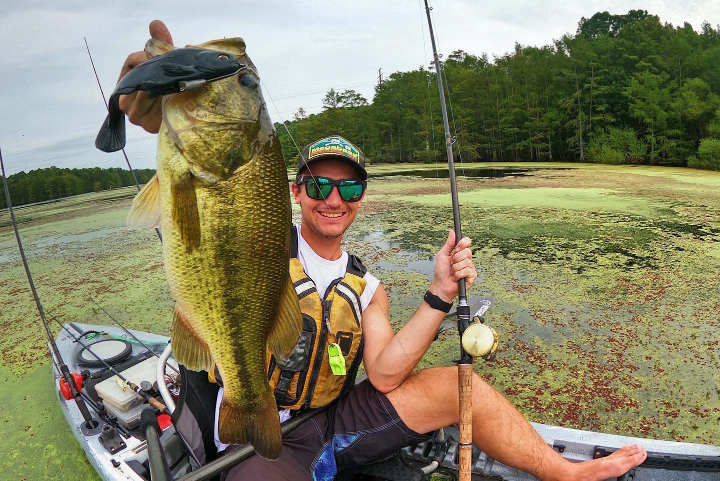 man holds up a largemouth bass caught from a kayak with a swimbait lure