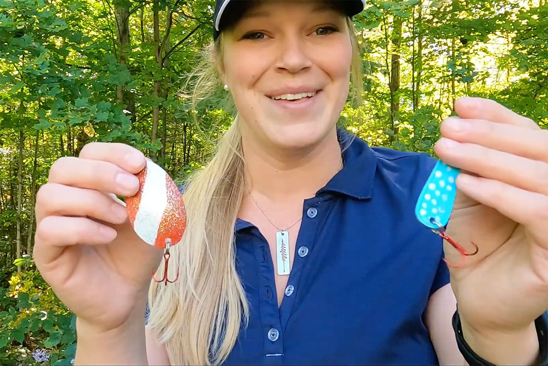 woman holds up finished DIY fishing spoons with split rings and treble hooks