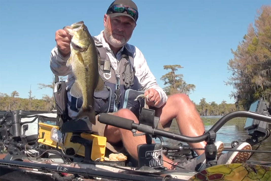 man holds up a bass caught while kayak fishing in Caddo Lake