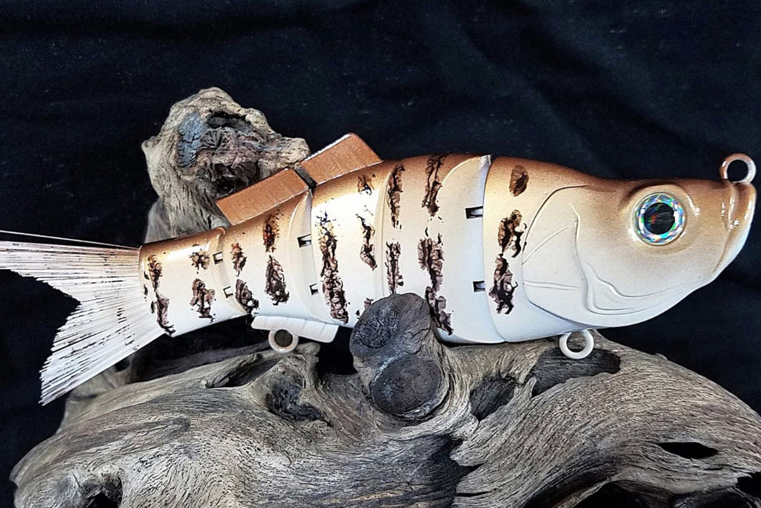 a large, hand-painted, jointed fishing lure on a piece of driftwood