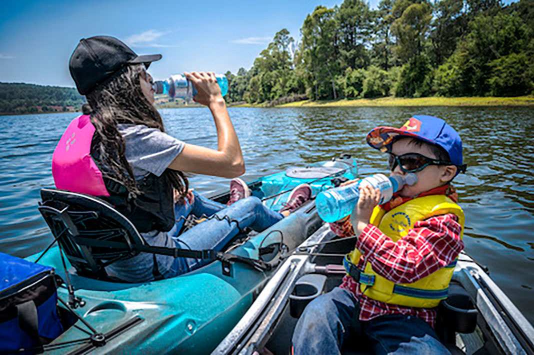 a boy and girl take drinks from their water bottles while they float on kayaks