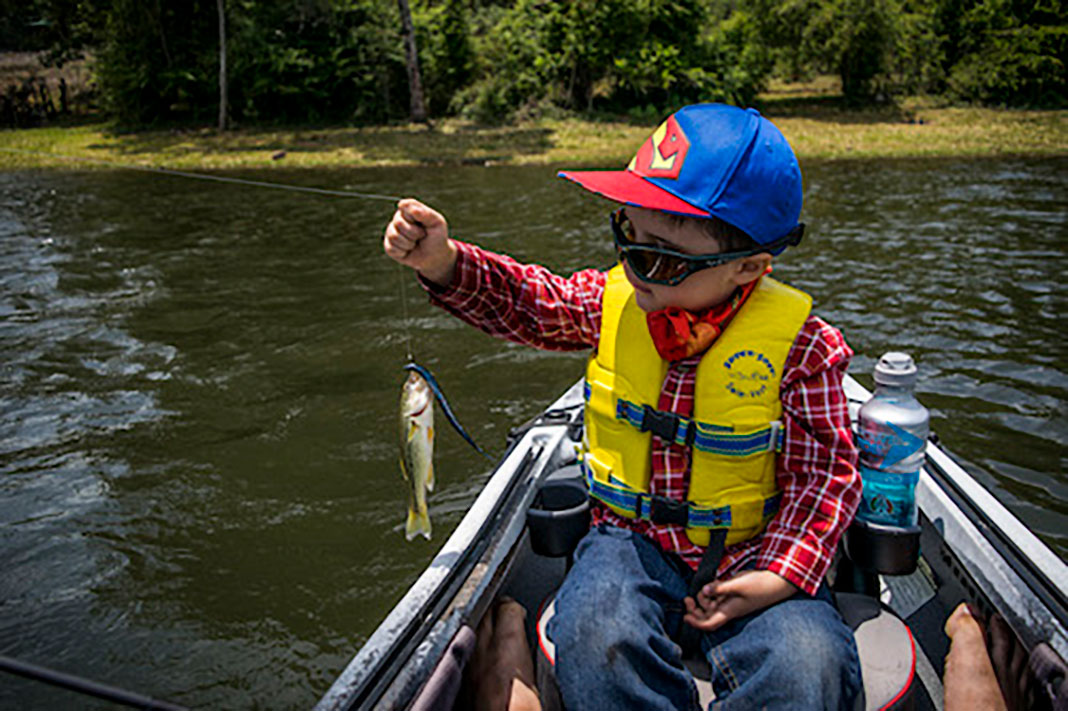 a boy holds up the first fish that he has caught