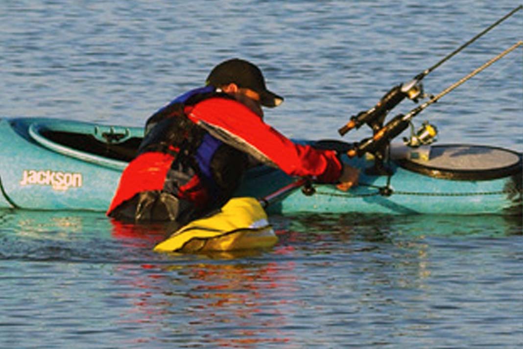 man uses an inflatable paddle float to complete an emergency winter sit-inside kayak re-entry