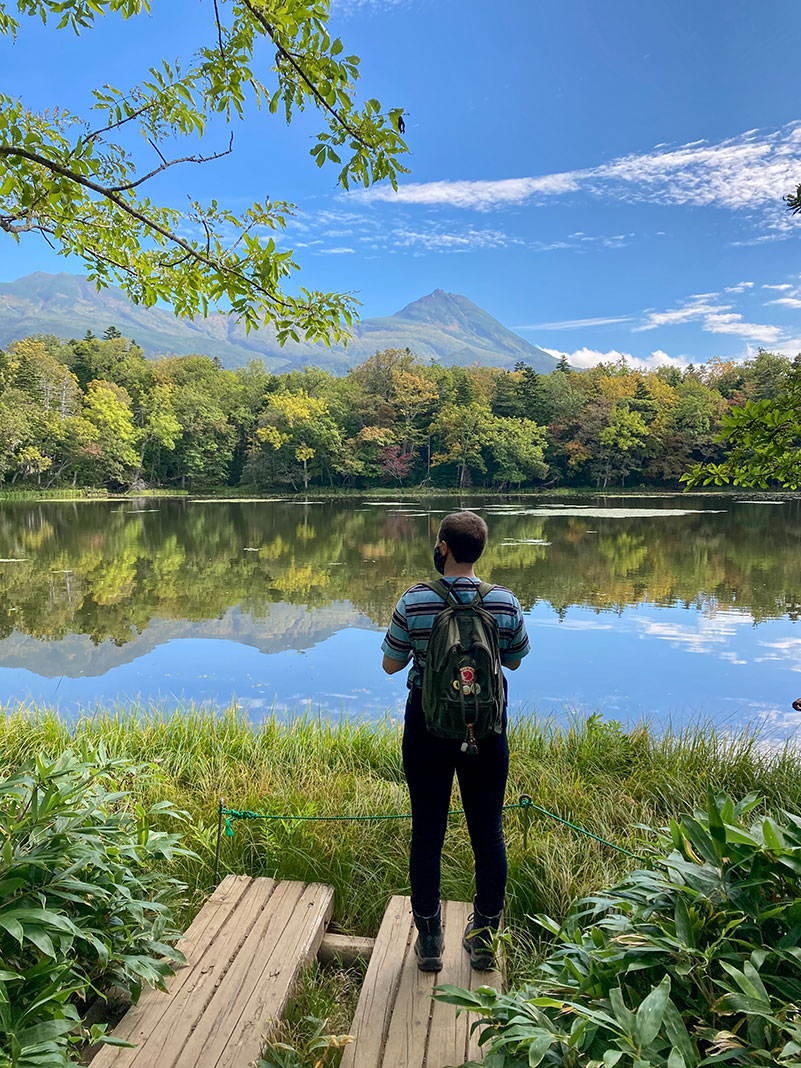 Man standing at edge of a lake with mountain in background.