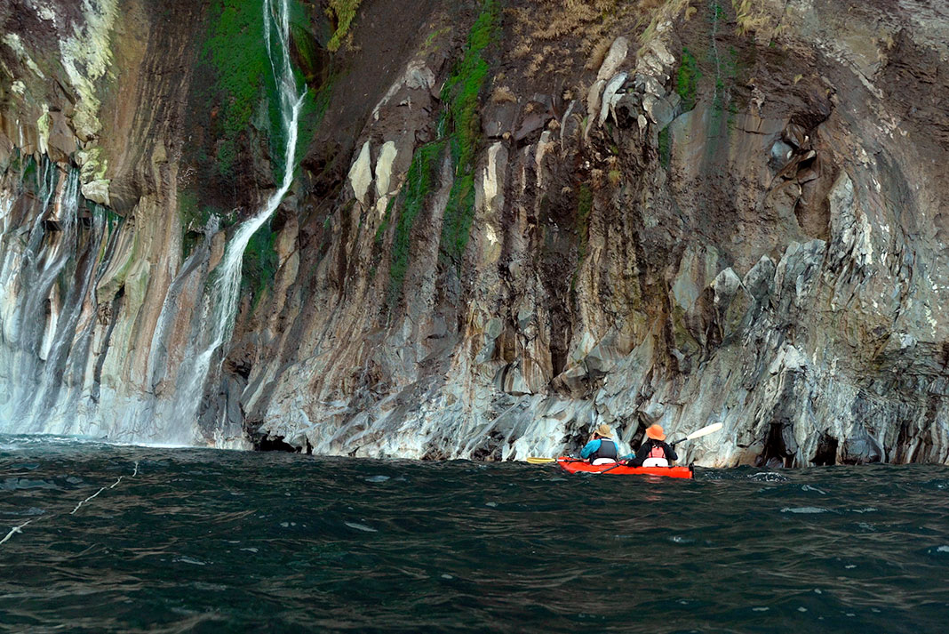 Tandem kayak next to cliff face with waterfall