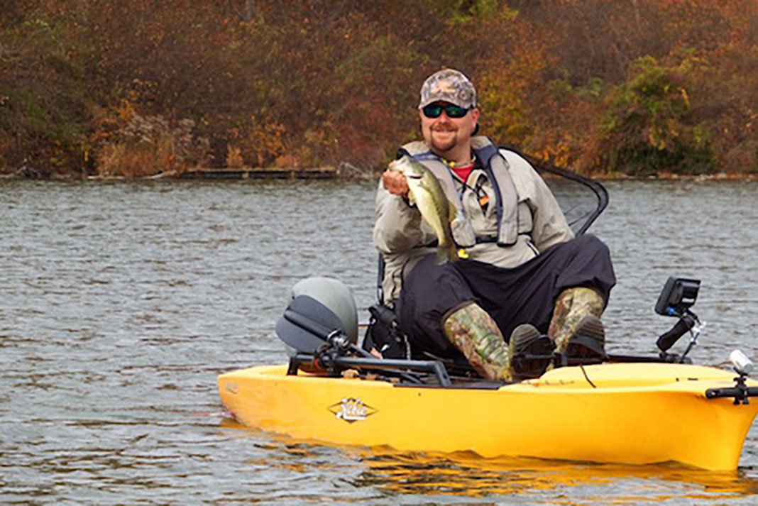 kayak angler in a yellow boat celebrates catching a bass during the fall season