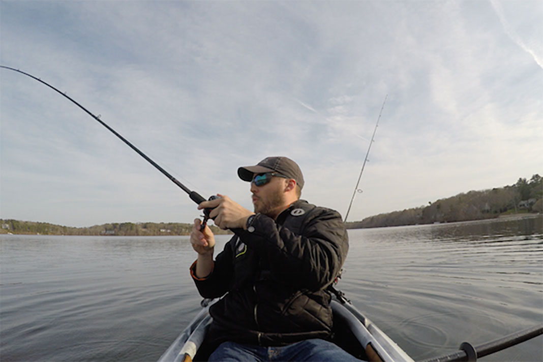 Man reels in a catch while seated in his fishing kayak