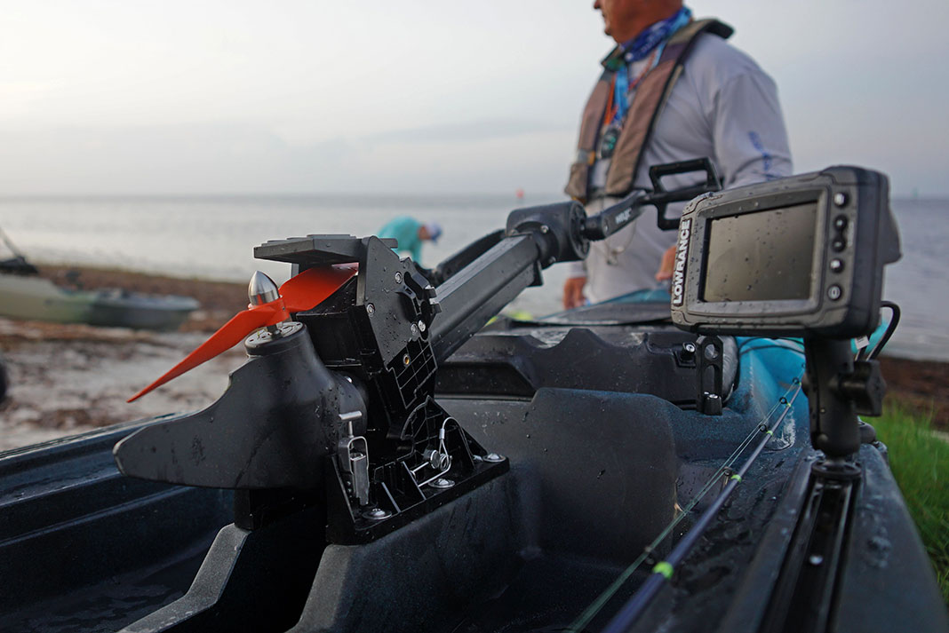 a pedal fishing kayak in the foreground with a fish finder and man in the background