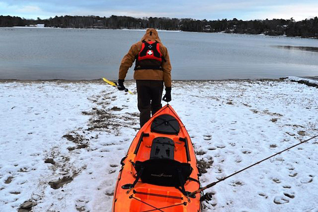 man drags kayak across snow during the fishing off-season