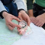 The Ultimate Guide To Using A Compass For Paddlers person moving the bezel on a compass, over a map with another person watching on.