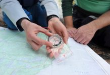 person moving the bezel on a compass, over a map with another person watching on.