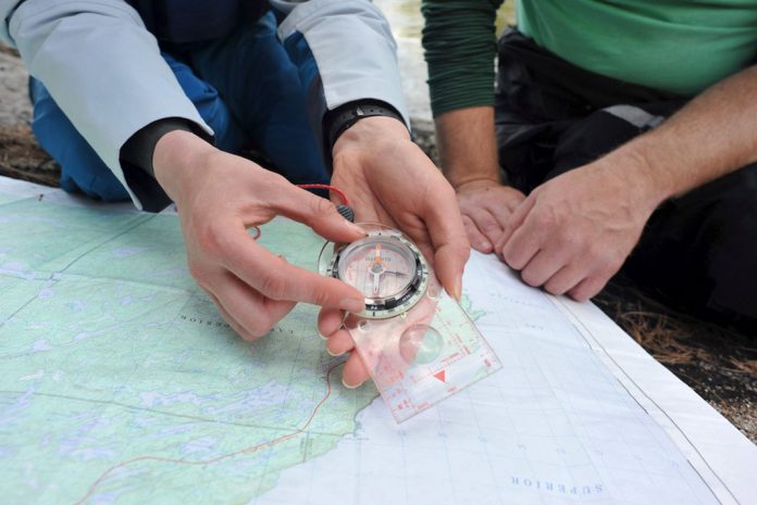 person moving the bezel on a compass, over a map with another person watching on.