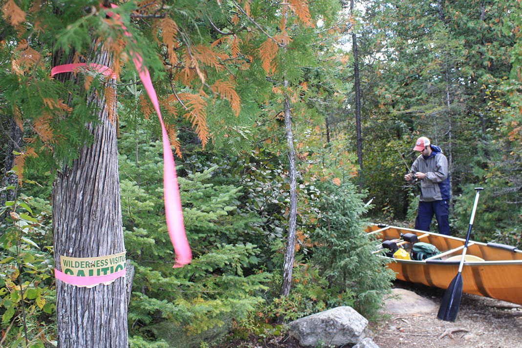 man stows fishing gear before starting a canoe portage