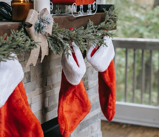 holiday stockings hung on a mantle in front of a lit-up Christmas tree