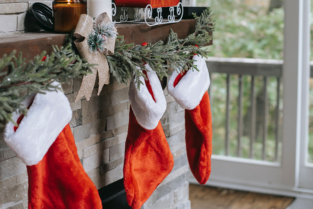 holiday stockings hung on a mantle in front of a lit-up Christmas tree