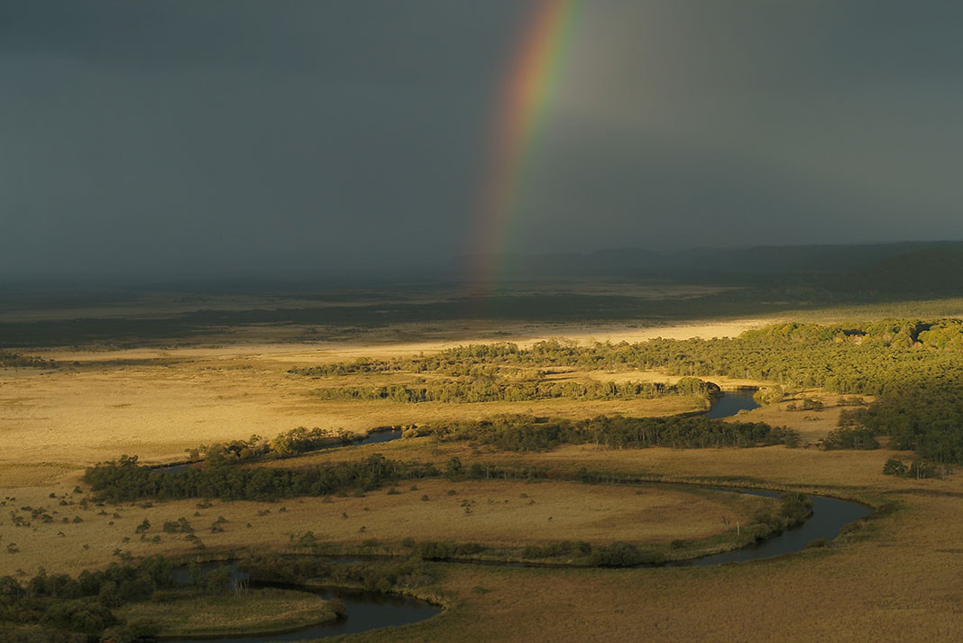 River flowing through marshland with rainbow in background