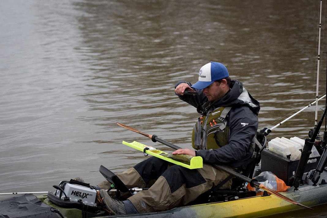 kayak angler takes a photo while measuring a fish on a fluorescent ruler