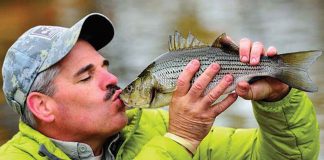 man in green coat holds up a fish and kisses it