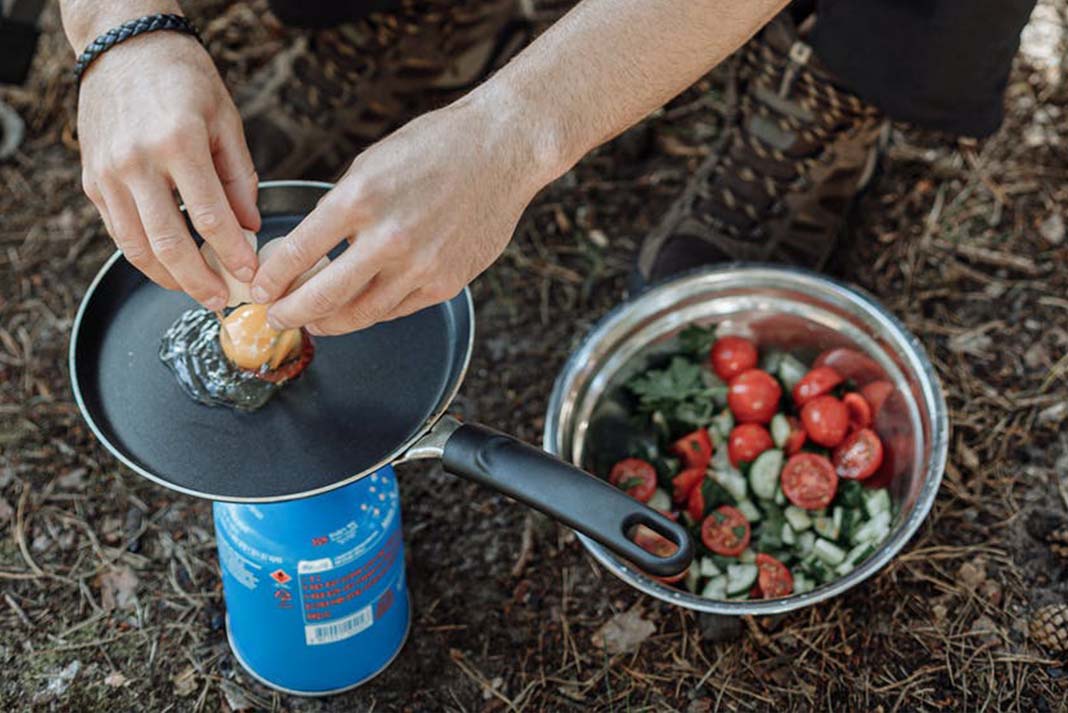 person cooking eggs on a portable camp burner with a salad nearby