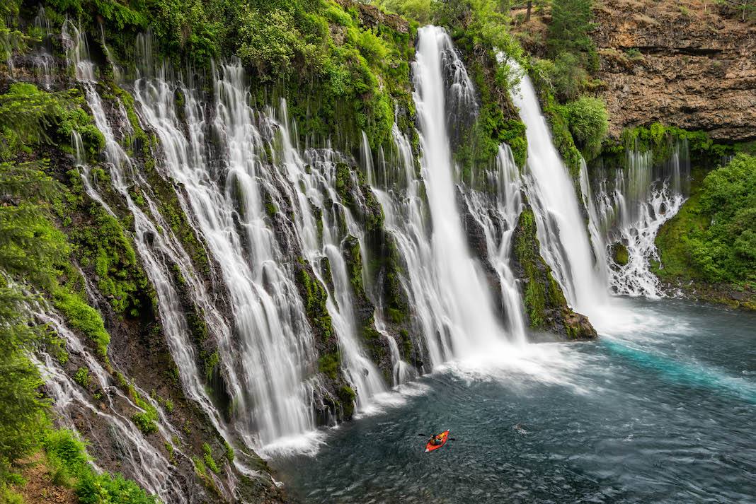 Inflatable kayak being paddled beside waterfall