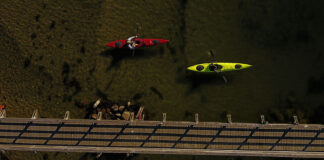 Overhead shot of green and red day touring kayaks paddling beside a wooden bridge