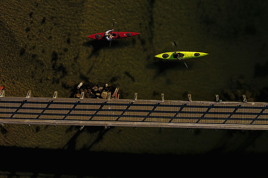 Overhead shot of green and red day touring kayaks paddling beside a wooden bridge