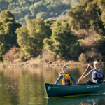 Read This Before Purchasing A Mad River Canoe Two people paddling dark green canoe