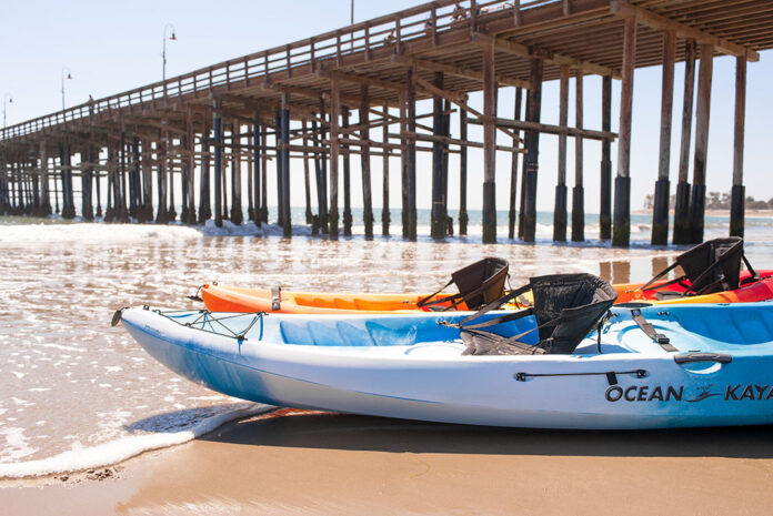 Two Ocean kayaks pulled up on the beach with pier in background.