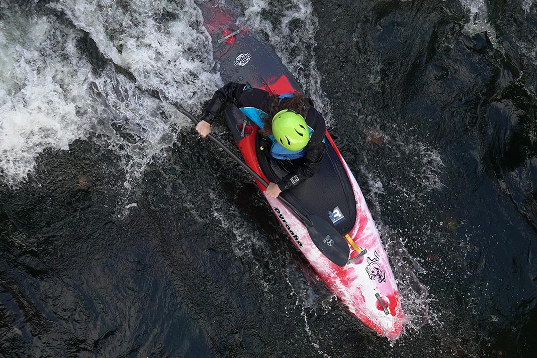Overhead shot of someone paddling a whitewater kayak through a wave
