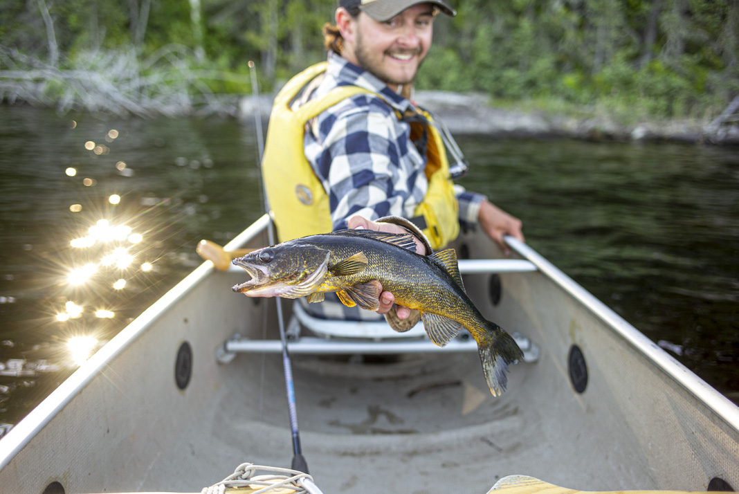 Man turned around in bow of canoe holding fish