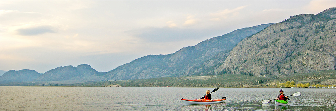 Two people paddling touring kayaks with mountains in background